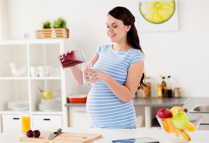 Pregnant woman holding a fresh plum, showcasing its safety for consumption during pregnancy.